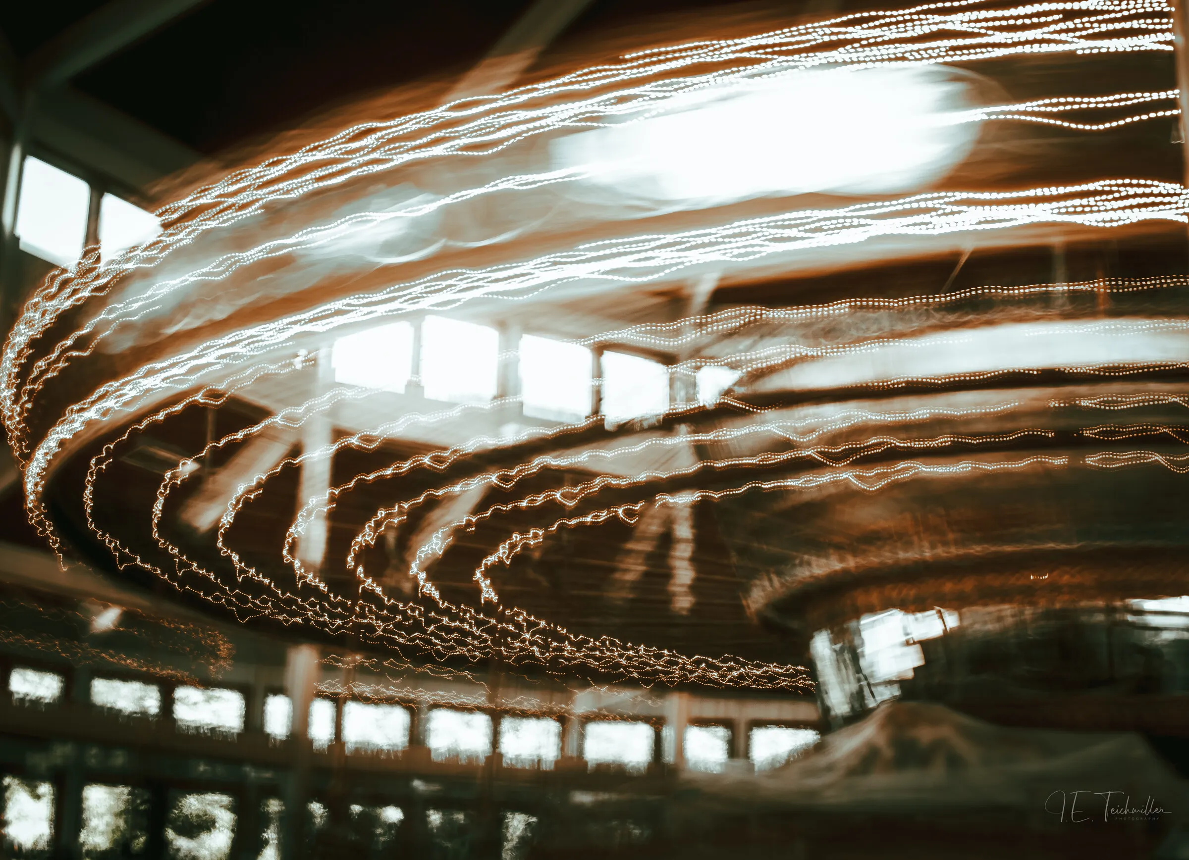 Long-exposure light painting: ribbons of warm light swirling in arcs beneath the windows of a darkened barn.